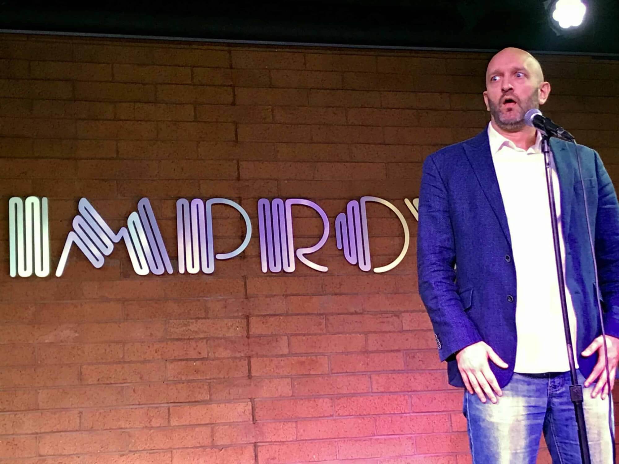 Paul doing a funny face next to the mic. On stage at an improv show.